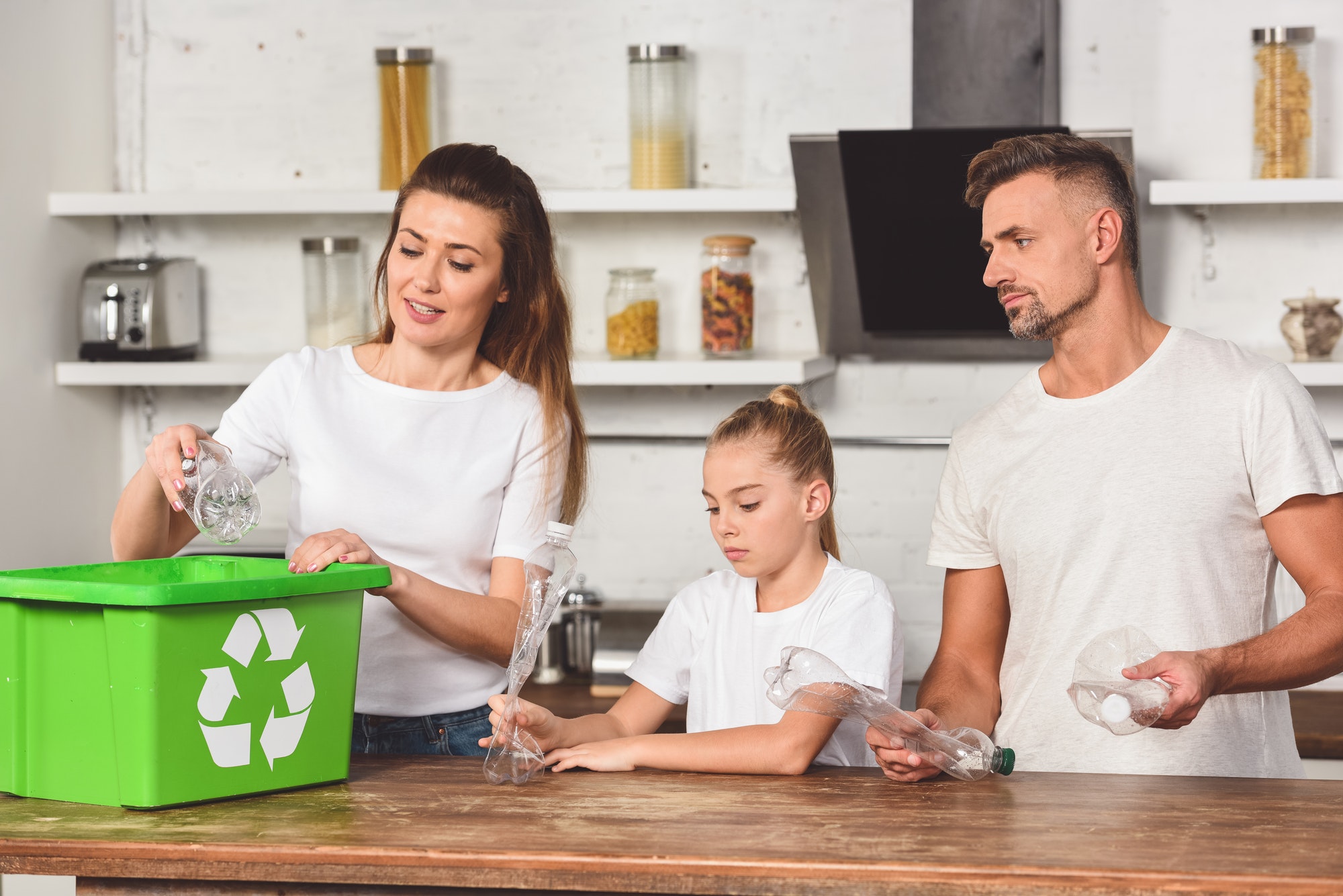 family standing at kitchen and putting empty plastic bottles in recycle box